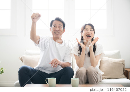 明るい部屋でスポーツや楽しいテレビを見ながらガッツポーズをする夫婦 正面のクローズアップ 明るい部屋でスポーツや楽しいテレビを見ながらガッツポーズをする夫婦 正面のクローズアップ 116407022