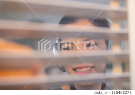 Excited young asian woman with headphones singing and dancing while dusting a window. 116408278