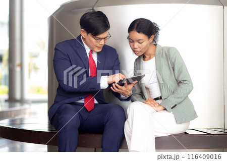 Two young business man and woman in formal meeting and discussing documents and using a tablet. 116409016