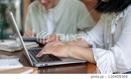 A close-up image of a woman working on her laptop computer while discussing work with her colleague. A close-up image of a woman working on her laptop computer while discussing work with her colleague. 116409366