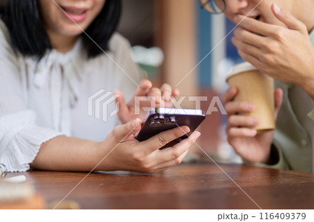 Two happy Asian friends are enjoying talking while watching a video on a smartphone together. 116409379