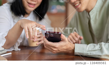 Two happy Asian friends are enjoying talking while watching a video on a smartphone together. 116409381