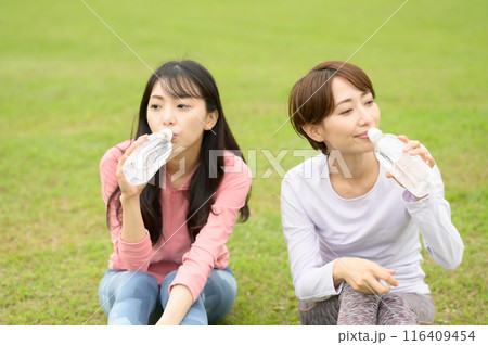 運動後に芝生の上で水分補給する二人の女性 運動後に芝生の上で水分補給する二人の女性 116409454