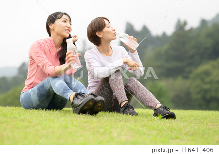 運動後に芝生の上で水分補給する二人の女性 116411406