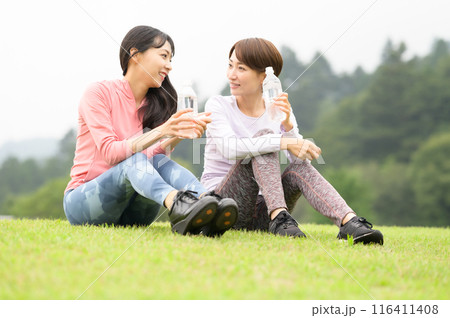 運動後に芝生の上で水分補給する二人の女性 116411408