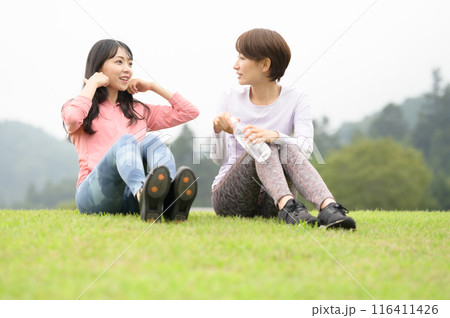 運動後に芝生の上で水分補給する二人の女性 116411426