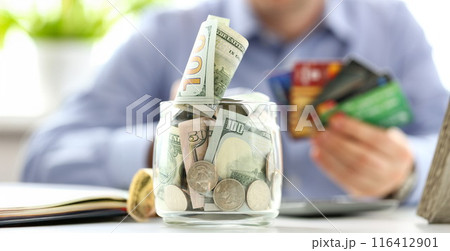 Big jar full of money stand at working table with male hand holding bunch of credit cards 116412901