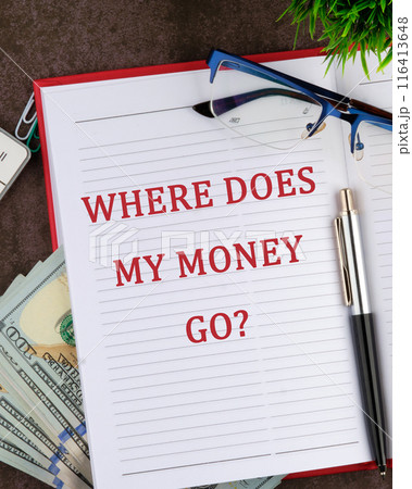 Text written WHERE DOES MY MONEY GO in a red business notebook in a composition with money and glasses Text written WHERE DOES MY MONEY GO in a red business notebook in a composition with money and glasses 116413648