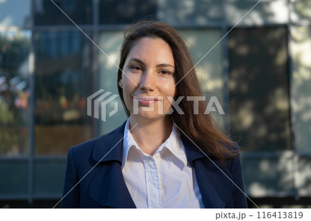 Portrait of an attractive strong confident independent woman in a blue suit standing against the background of a business building and looking at the camera Portrait of an attractive strong confident independent woman in a blue suit standing against the background of a business building and looking at the camera 116413819