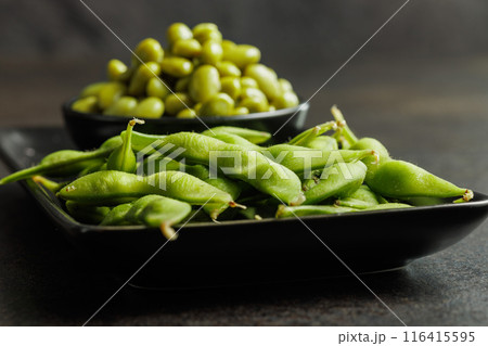 Green edamame pods. Fresh soybeans on plate on black table. Green edamame pods. Fresh soybeans on plate on black table. 116415595