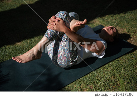 Woman practicing yoga outdoors, stretching and relaxing on yoga mat in the sunlight Woman practicing yoga outdoors, stretching and relaxing on yoga mat in the sunlight 116417190