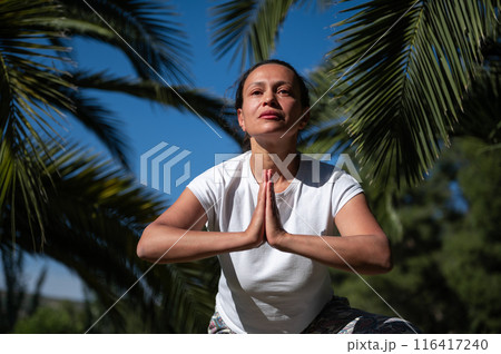 Woman practicing yoga outdoors in a peaceful environment surrounded by palm trees 116417240