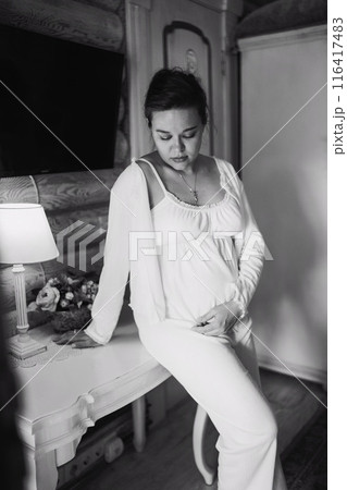 Calm and beautiful young pregnant woman in white pajamas in bedroom Calm and beautiful young pregnant woman in white pajamas in bedroom 116417483