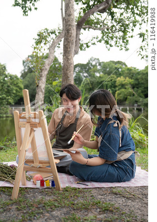 Romantic Picnic Couple Drawing Outdoors in Nature with Easel and Painting, Capturing Creative Moments in a Serene Park Setting 116419988