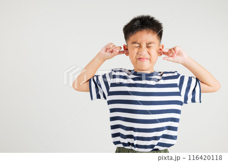 Asian young kid boy expression of pain and frustration is evident as she covers ears and closes her eyes with fingers to escape the loud noise in studio shot isolated white background, primary child Asian young kid boy expression of pain and frustration is evident as she covers ears and closes her eyes with fingers to escape the loud noise in studio shot isolated white background, primary child 116420118