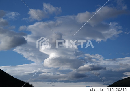 Majestic Dark Mountains with Wispy White Clouds and Lush Green Trees under Blue Sky 116420813