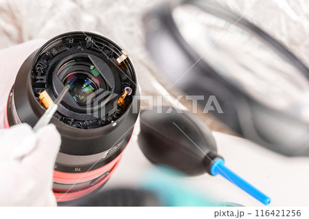 the hands of the master with gloves and a broken lens of a professional camera. 116421256
