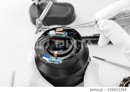 the hands of the master with gloves and a broken lens of a professional camera. 116421264