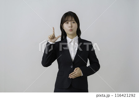 白背景のスーツを着た指でポーズをする若い女性のポートレート 116421292