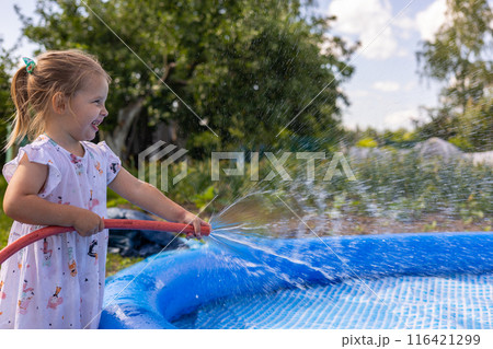 While drawing water into the pool, a happy child closes the hose with his finger and splashes the water. When installing a pool, a lot of splashes fly in all directions. A child plays with water. 116421299