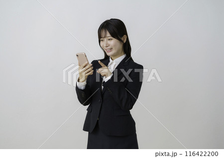 白背景のスーツを着てスマホをクリックする若い女性のポートレート 116422200
