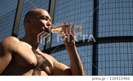 Athletes handsome sun-tanned shirtless man drinking water on outdoor sports ground. Concept water balance for hot season for active workout. Banner. Close up. Athletes handsome sun-tanned shirtless man drinking water on outdoor sports ground. Concept water balance for hot season for active workout. Banner. Close up. 116422466