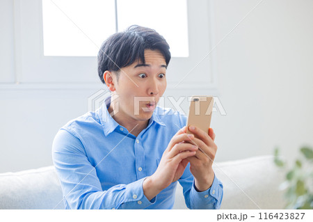 スマホを見ながら驚く青年 116423827