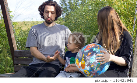 Dad, mom and little boy swinging on bench swing at playground. Family lifestyle. Kids and activity. Dad, mom and little boy swinging on bench swing at playground. Family lifestyle. Kids and activity. 116423949