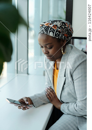 Focused Woman Checking Phone by Office Window 116424007
