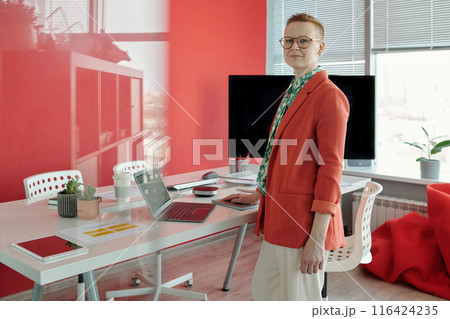 Portrait Of Female Office Worker Standing By Desk With Laptop 116424235