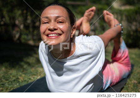 Smiling woman practicing yoga outdoors on sunny day with focus on fitness and well-being 116425275