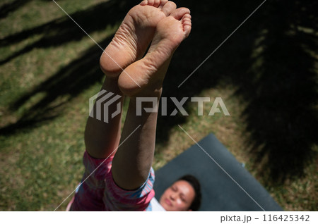 Woman practicing yoga outdoors performing a leg raise pose on a sunny day 116425342