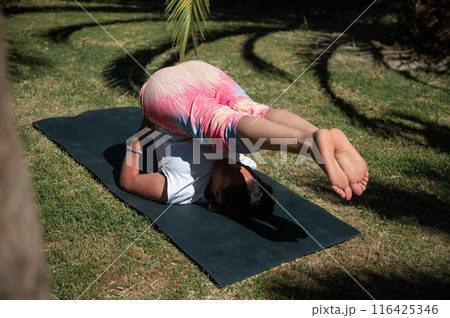 Woman practicing yoga outdoors on a sunny day performing challenging pose on yoga mat 116425346