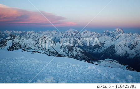 Sunset hues bathe Caucasus Range, peaks covered in snow. Orange and pink sky above frosty mountain tops. Alpine landscape at dusk, serene nature view. Sunset hues bathe Caucasus Range, peaks covered in snow. Orange and pink sky above frosty mountain tops. Alpine landscape at dusk, serene nature view. 116425893