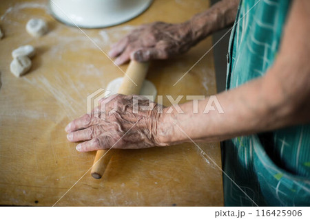 Elderly woman rolls dough for vareniki on kitchen table. Traditional Ukrainian cuisine, homemade pierogi making process. Granny prepares authentic Eastern European dish, culinary skills displayed. Elderly woman rolls dough for vareniki on kitchen table. Traditional Ukrainian cuisine, homemade pierogi making process. Granny prepares authentic Eastern European dish, culinary skills displayed. 116425906