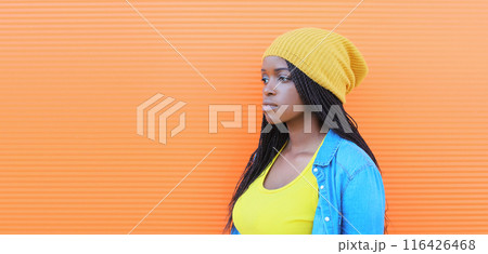 stylish modern African teenage girl in yellow hat, casual clothing looking away on orange background stylish modern African teenage girl in yellow hat, casual clothing looking away on orange background 116426468