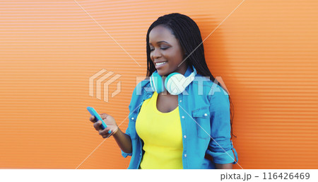 Happy african woman listening to music with smartphone, black girl smiles in headphones holds phone 116426469