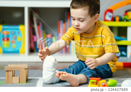 A little toddler boy holds his leg in a cast with his hands. Fracture of a foot and finger in children. Human healthcare and medicine concept. Bandage A little toddler boy holds his leg in a cast with his hands. Fracture of a foot and finger in children. Human healthcare and medicine concept. Bandage 116427889