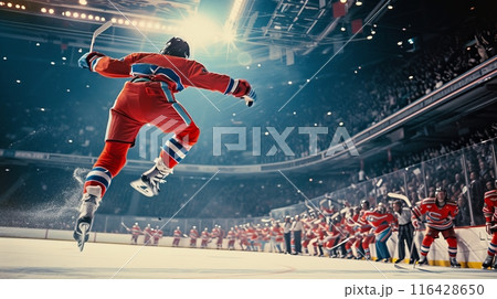 A hockey player in a red jersey leaps joyfully after scoring a goal, with the crowd cheering in the background. 116428650
