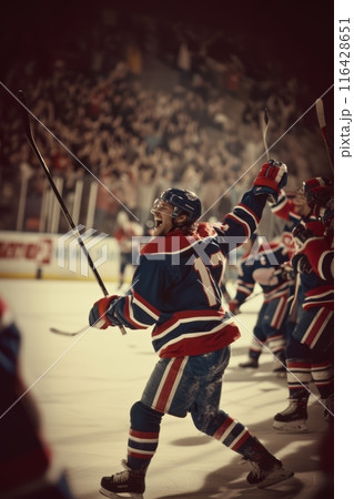 Hockey player in red celebrating a win with fists pumped in the air, illuminated by the spotlight. 116428651