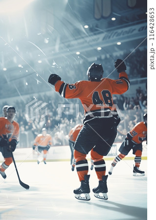 Hockey player in red celebrating a win with fists pumped in the air, illuminated by the spotlight. 116428653