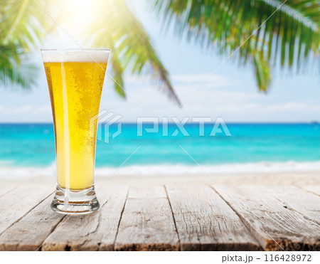 Glass of beer on a table with a stunning sea and beach background 116428972