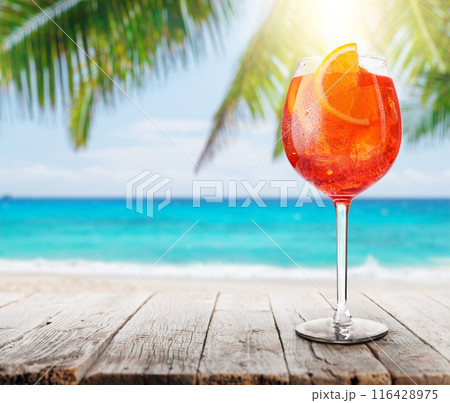 Glass of Aperol Spritz on a table with a stunning sea and beach background Glass of Aperol Spritz on a table with a stunning sea and beach background 116428975