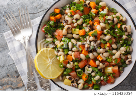 Winter salad with black-eyed beans, carrots, onions, tomatoes, basil, parsley dressed with olive oil closeup on the plate. Horizontal top view 116429354