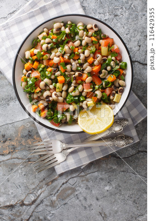 Black-eyed bean salad with carrots, onions, tomatoes, basil, parsley dressed with olive oil closeup on the plate. Vertical top view 116429355