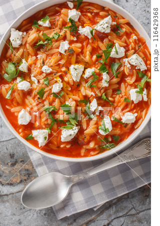 Mediterranean cuisine orzo pasta with spicy tomato sauce, feta, garlic, onion, carrots closeup on the plate on the table. Vertical top view 116429368