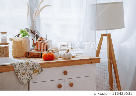 Bright kitchen with wooden furniture with kitchen utensils and three decorative pumpkins. Bright kitchen with wooden furniture with kitchen utensils and three decorative pumpkins. 116429533