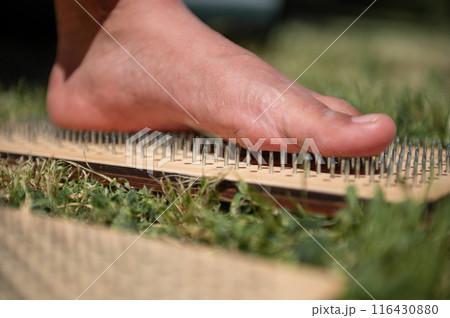 Close-up of bare foot stepping on a bed of nails, outdoors on grass Close-up of bare foot stepping on a bed of nails, outdoors on grass 116430880