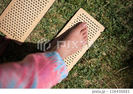 Close-up of a person practicing reflexology with wooden foot massage boards on grass Close-up of a person practicing reflexology with wooden foot massage boards on grass 116430881