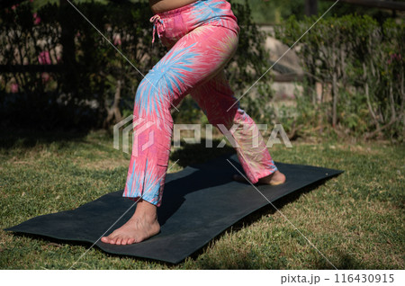 Woman practicing yoga outdoors on a sunny day wearing colorful pants 116430915
